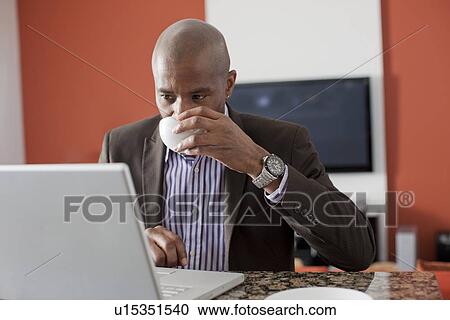 Stock Image - Man enjoying coffee while using laptop. Fotosearch