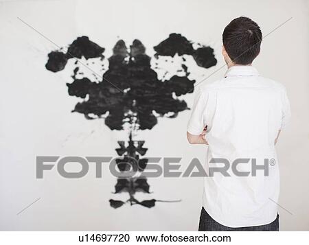 Stock Image - Man looking at black complex shape painted on wall. Fotosearch