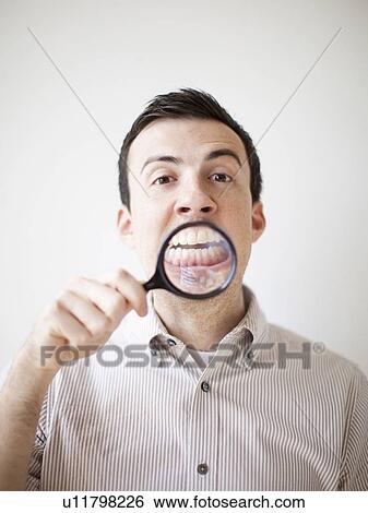 Stock Photograph - Man looking standing looking through magnifying glass. Fotosearch