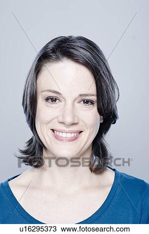 Stock Image - Mid adult woman smiling, studio shot. Fotosearch