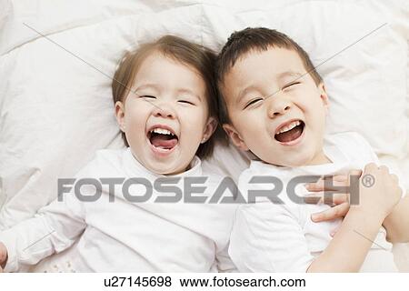 Stock Photo - Mixed race siblings (2-3, 4-5) lying in bed side by side. Fotosearch