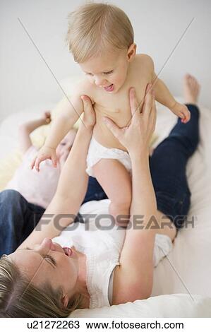 Stock Image - Mother and children (6-11 moths, 2-3) lying in bed. Fotosearch