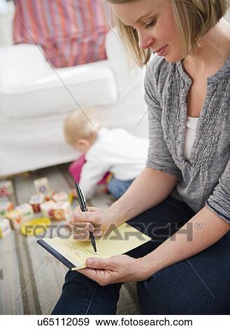 Mother doing notes, son (6-11 months) playing in background View Large Photo Image Stock Photo - Mother doing notes, son (6-11 months) playing in background. Fotosearch
