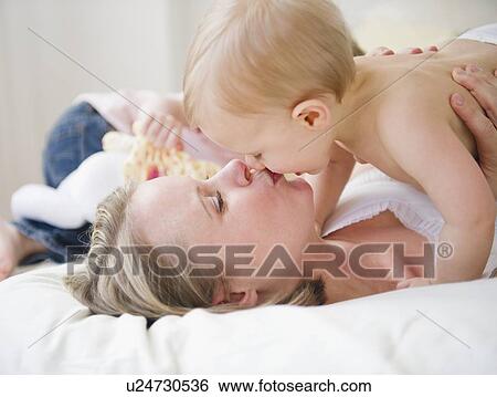 Stock Photograph - Mother kissing son (6-11 moths), daughter (2-3) in background . Fotosearch