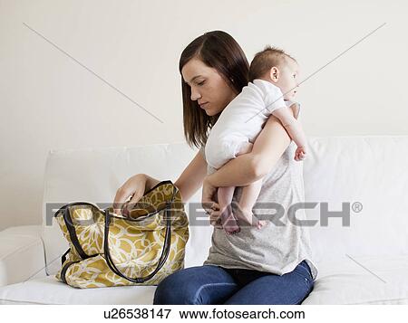 Stock Photo - Mother reaching in her handbag white embracing baby girl (2-5 months). Fotosearch