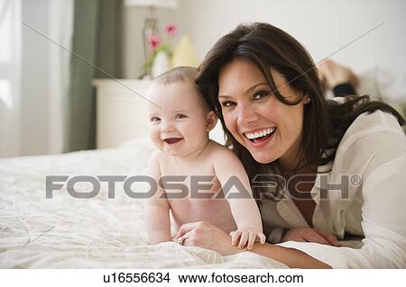 Mother with baby daughter (6-11 months) lying on bed View Large Photo Image Picture - Mother with baby daughter (6-11 months) lying on bed. Fotosearch