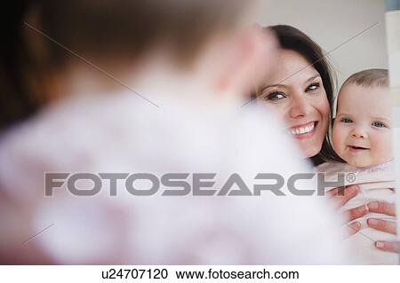 Stock Image - Mother with baby daughter (6-11 months) reflecting in mirror. Fotosearch
