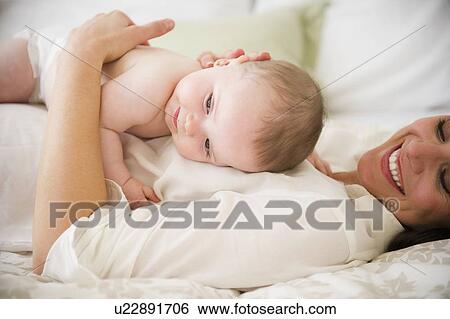 Mother with baby daughter (6-11 months) lying on bed View Large Photo Image Stock Photograph - Mother with baby daughter (6-11 months) lying on bed. Fotosearch