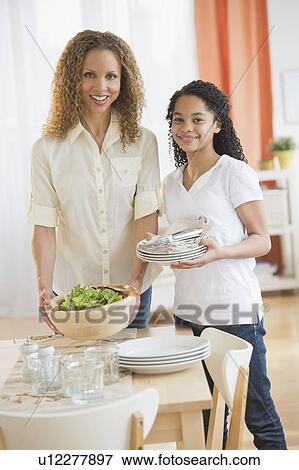 Stock Photo - Mother with daughter (10-11) setting table. Fotosearch