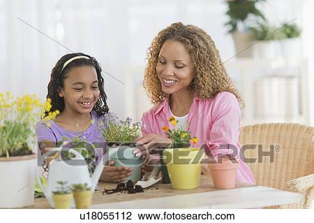 Stock Image - Mother with daughter (12-13) potting flowers. Fotosearch