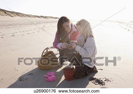 Mother with daughter collecting shells on beach View Large Photo Image Stock Photograph - Mother with daughter collecting shells on beach. Fotosearch