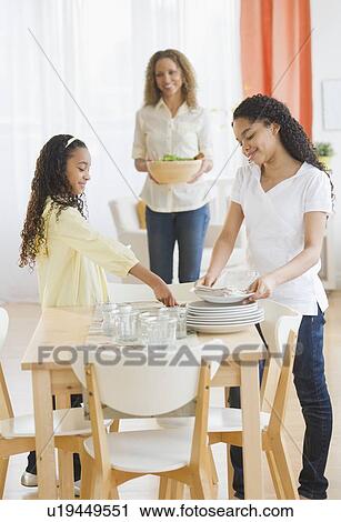 Stock Image - Mother with daughters (10-13) setting table. Fotosearch