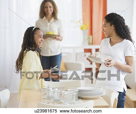 Stock Photography - Mother with daughters (10-13) setting table. Fotosearch
