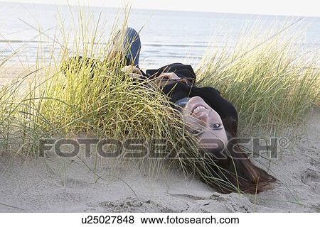 Stock Photo - Netherlands, Zeeland, Haamstede, Woman lying on sand dune. Fotosearch