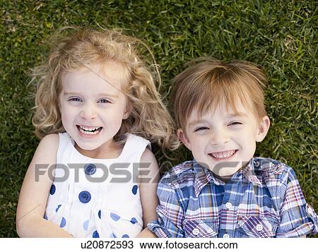 Stock Image - Outdoor portrait of girl (4-5) and boy (6-7) lying on grass. Fotosearch