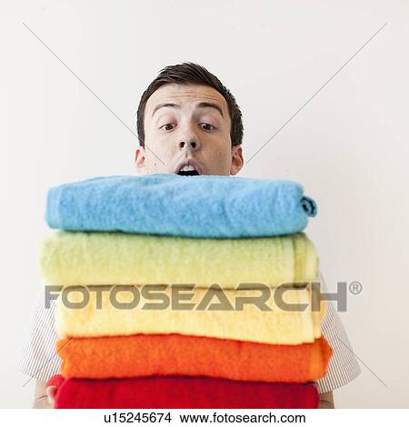 Overburdened young man holding stack of multi-coloured towels View Large Photo Image Picture - Overburdened young man holding stack of multi-coloured towels. Fotosearch