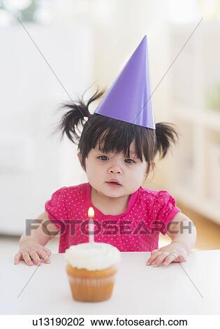 Portrait of baby girl (12-17 months) in party hat with cupcake View Large Photo Image Stock Image - Portrait of baby girl (12-17 months) in party hat with cupcake. Fotosearch