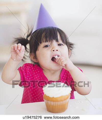 Portrait of baby girl (12-17 months) in party hat eating cupcake View Large Photo Image Stock Photograph - Portrait of baby girl (12-17 months) in party hat eating cupcake. Fotosearch