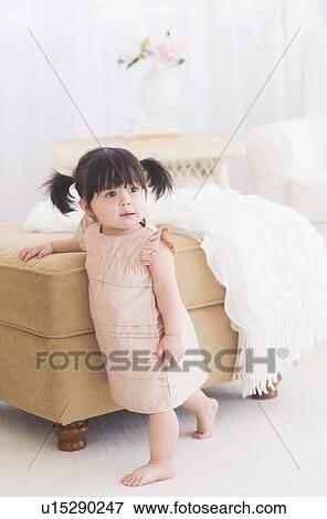 Portrait of baby girl (12-17 months) standing near sofa View Large Photo Image Stock Photo - Portrait of baby girl (12-17 months) standing near sofa. Fotosearch
