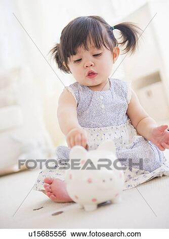 Stock Photograph - Portrait of baby girl (12-17 months) playing with piggy bank. Fotosearch