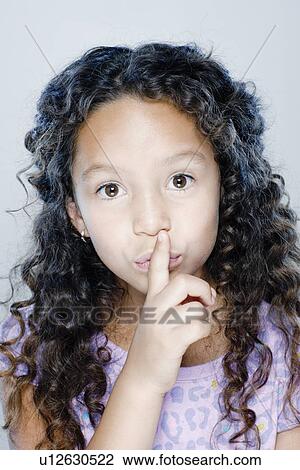 Stock Image - Portrait of girl (8-9) with finger on her lips, studio shot. Fotosearch