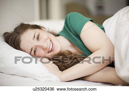 Portrait of happy young woman lying in bed View Large Photo Image Stock Photograph - Portrait of happy young woman lying in bed. Fotosearch