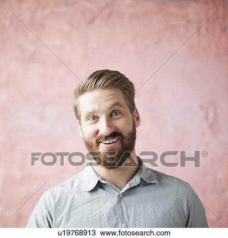 Stock Image - Portrait of laughing young man against pin background. Fotosearch