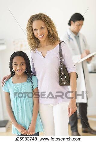 Stock Photo - Portrait of mother with daughter (12-13) at doctor's office. Fotosearch