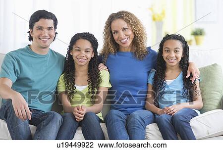 Stock Image - Portrait of parents with daughters (10-13) sitting on sofa. Fotosearch