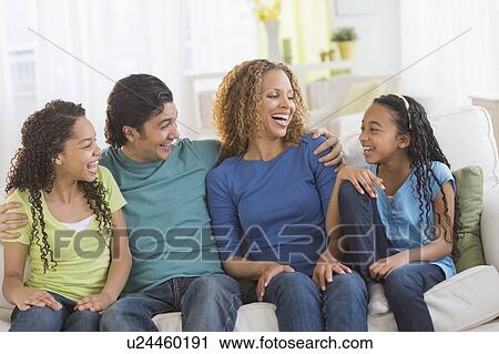 Stock Image - Portrait of parents with daughters (10-13) sitting on sofa. Fotosearch
