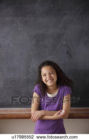 Stock Image - Portrait of schoolgirl (10-11) standing in front of blackboard. Fotosearch