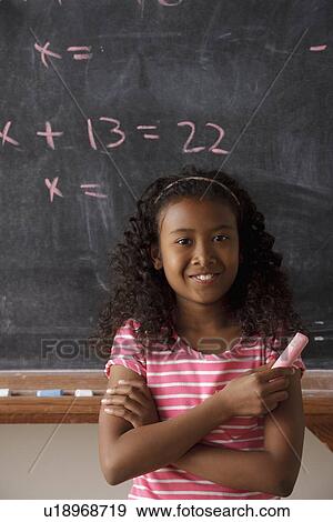 Stock Photo - Portrait of schoolgirl (10-11) standing in front of blackboard during math classes. Fotosearch