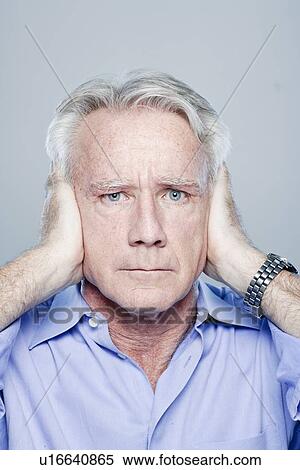 Stock Photography - Portrait of senior man covering his ears, studio shot. Fotosearch