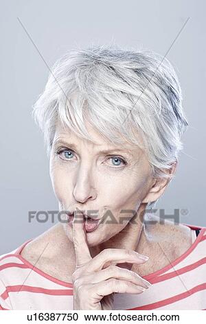 Stock Image - Portrait of senior woman with finger on her lips, studio shot. Fotosearch