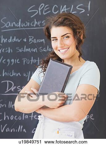 Stock Image - Portrait of smiling waitress against blackboard with menu. Fotosearch