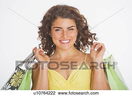 Stock Image - Portrait of smiling woman carrying shopping bags, studio shot. Fotosearch