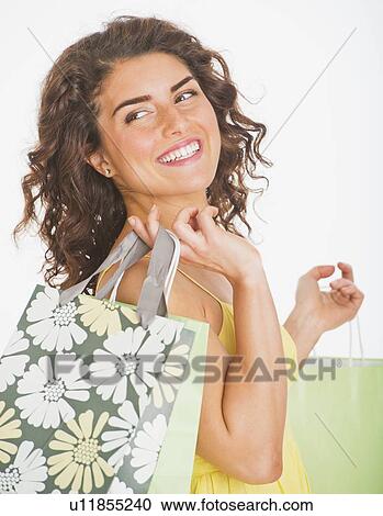 Stock Image - Portrait of smiling woman carrying shopping bags, studio shot. Fotosearch