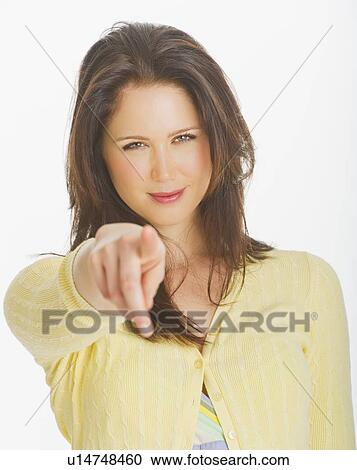 Stock Image - Portrait of smiling young woman pointing with finger, studio shot. Fotosearch