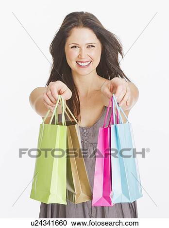 Stock Image - Portrait of smiling young woman with shopping bags, studio shot. Fotosearch