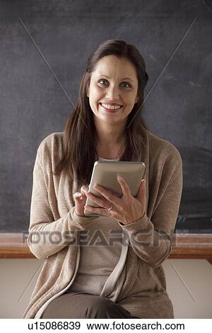 Stock Photo - Portrait of teacher in classroom holding digital tablet. Fotosearch