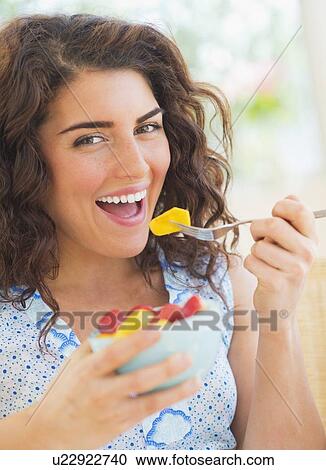 Stock Image - Portrait of woman eating fruit salad. Fotosearch