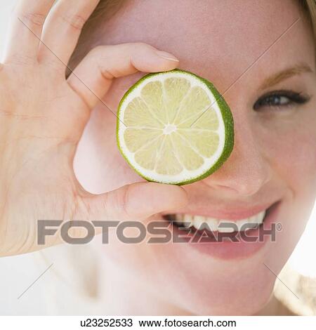 Stock Image - Portrait of woman holding slice of lime. Fotosearch