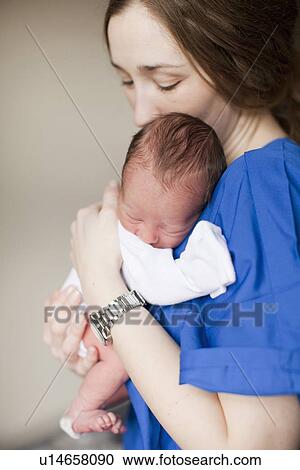 Stock Image - Portrait of young female nurse holding baby boy (2-5 months). Fotosearch