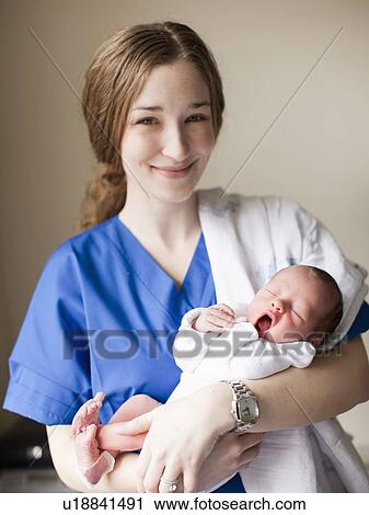 Stock Image - Portrait of young female nurse holding baby boy (2-5 months). Fotosearch