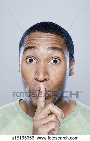 Portrait of young man with finger on his lips, studio shot View Large Photo Image Stock Photograph - Portrait of young man with finger on his lips, studio shot. Fotosearch