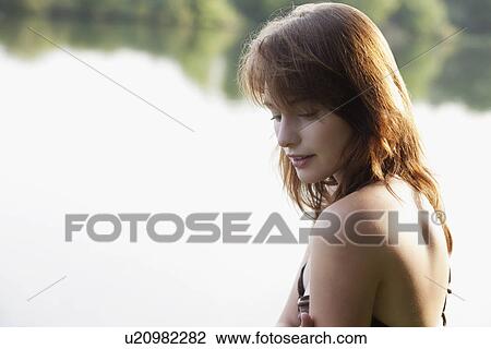 Stock Image - Portrait of young woman against lake. Fotosearch