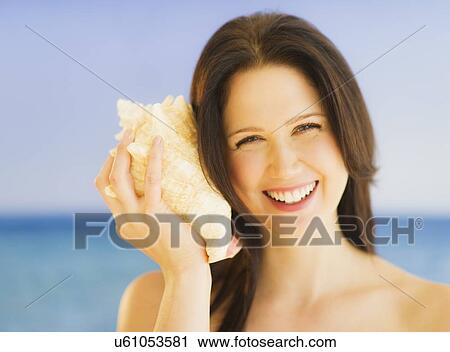 Portrait of young woman listening to seashell, studio shot View Large Photo Image Stock Image - Portrait of young woman listening to seashell, studio shot. Fotosearch