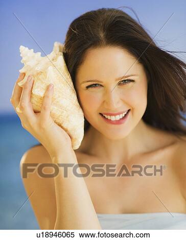 Portrait of young woman listening to seashell, studio shot View Large Photo Image Stock Photography - Portrait of young woman listening to seashell, studio shot. Fotosearch