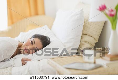 Stock Image - Portrait of young woman lying in bed. Fotosearch