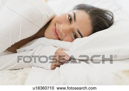 Stock Image - Portrait of young woman lying in bed. Fotosearch